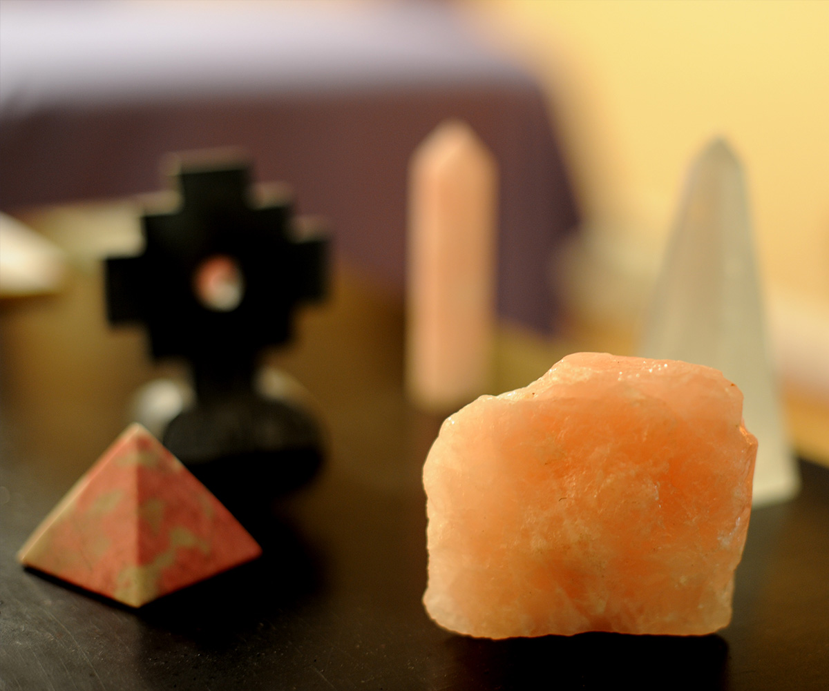 The image displays a collection of crystals and stones, including a prominent pink crystal and smaller items on a black surface.